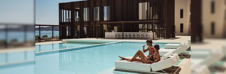Two people lounging on a poolside lounger at a Domes Resorts hotel.