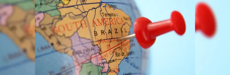 A red pin pushed into Brazil on a world globe.