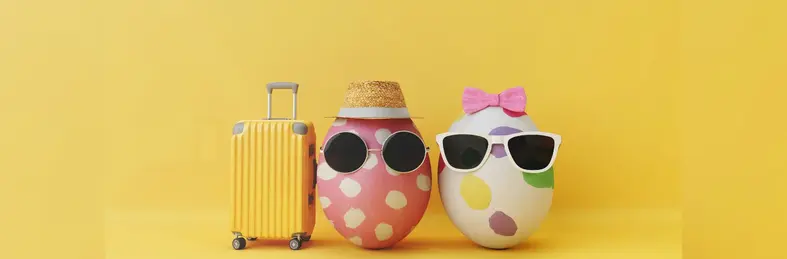 Two eggs painted and decorated wearing sunglasses, next to a suitcase.