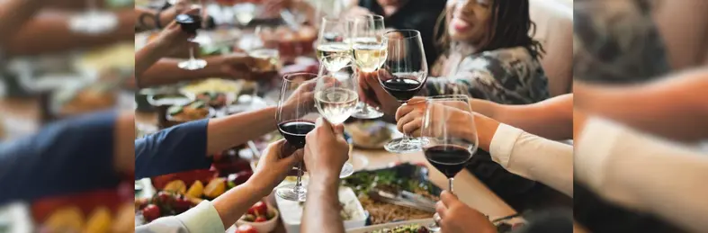 People eating brunch in a restaurant raising glasses of red and white wine to cheers.