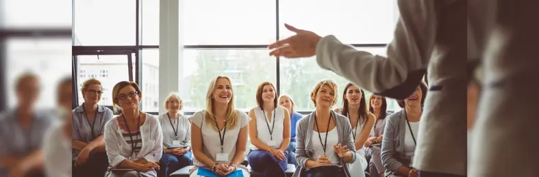 A businessperson in a grey suit delivering training to a room of female businesswomen.