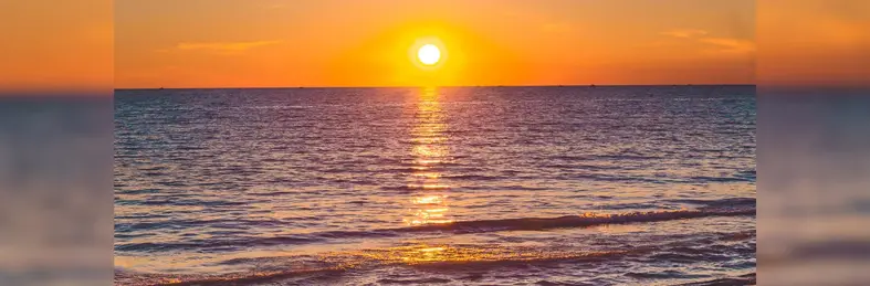 The blue sea against an orange sky near sunset.