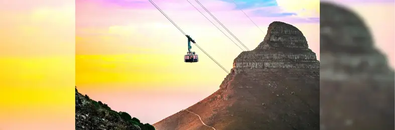 Image of a cabel car descending down Table Mountain in South Africa against a sunset backdrop