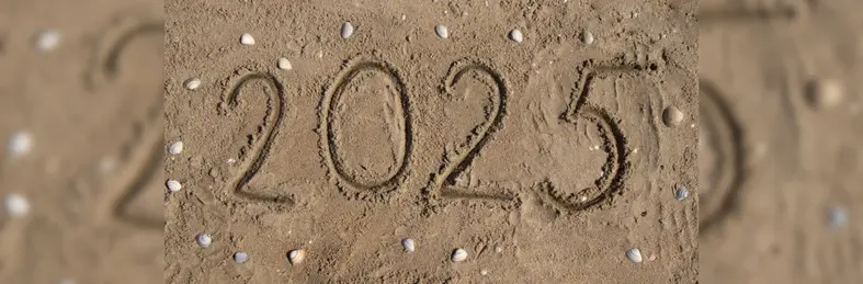 The numbers '2025' drawn in the sand, surrounded by pebbles and seashells.