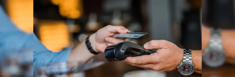 A person wearing a watch holding a card payment terminal to another person.