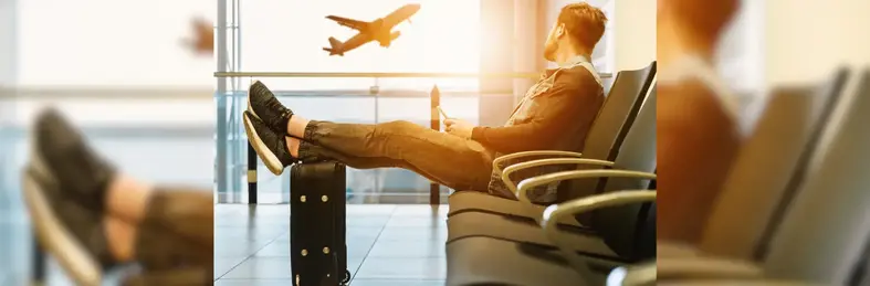 Man sitting in a departure lounge looking out the window towards a plane in the air
