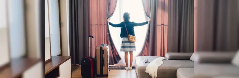 Lady looking out of the window with her suitcases in a hotel