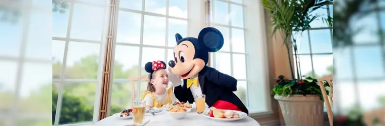 A child in Minnie ears posing with Mickey Mouse at a character dining experience at Walt Disney World, Florida.