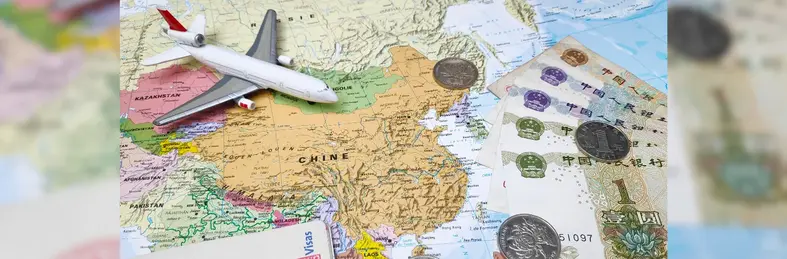 Composition made of a world map centered in East Asia with on it, some Chinese banknotes and coins as well as a toy plane and an opened passport with Chinese entry and exit stamps.