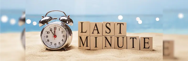 An alarm clock at 11:55 on the beach next to wooden letter blocks spelling out the words 'Last Minute'