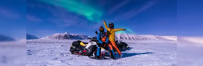 Two people on a snowmobile in Lapland with the Northern Lights in the background.