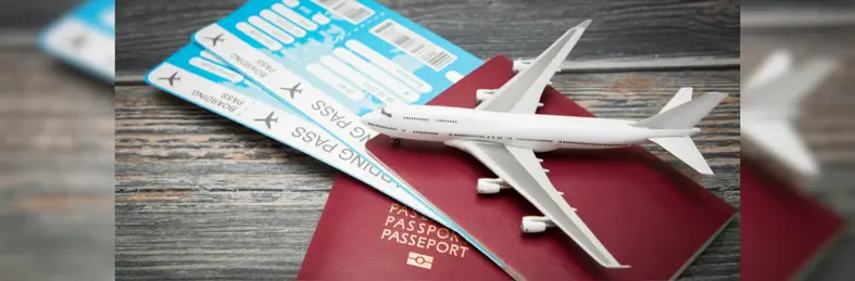 Two passports with boarding passes in them on a grey wooden table, with a small model plane resting on top.