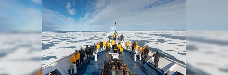 Guests on the bow of a ship sailing into the ice-covered seas of the Arctic
