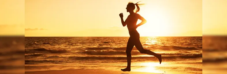 A silhouette of a woman running on a beach at sunset.