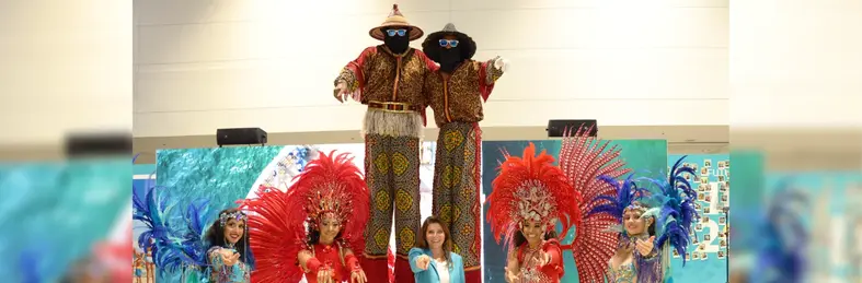 Stacy Ritter, president and CEO of Visit Lauderdale, with Caribbean carnival dancers and stilt walkers at IPW 2025.