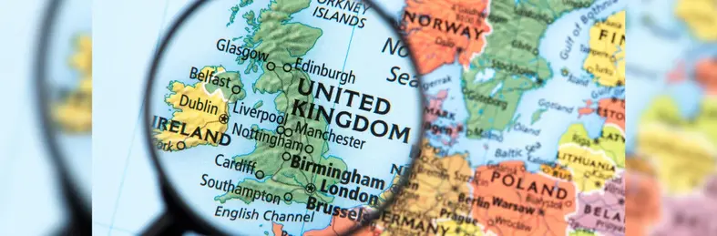 A magnifying glass examining the United Kingdom on a map of Europe.