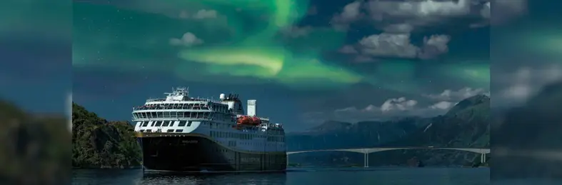 A Havila Voyages ship sailing underneath the Northern Lights