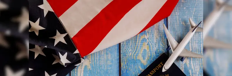 A flag of the USA, a model plane and a passport resting on a blue wooden table.