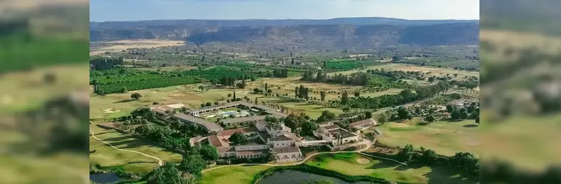 An aerial view of Dolce by Wyndham Siracusa, with rolling green hills and vegetation behind the property