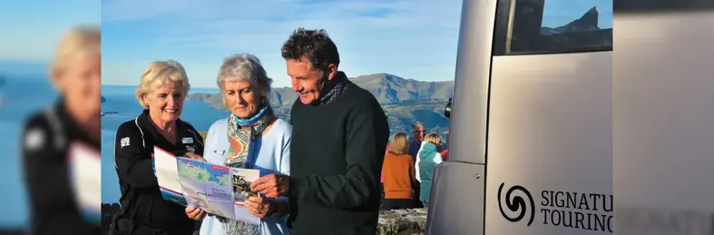 Three people on a coach tour in New Zealand looking at a map.
