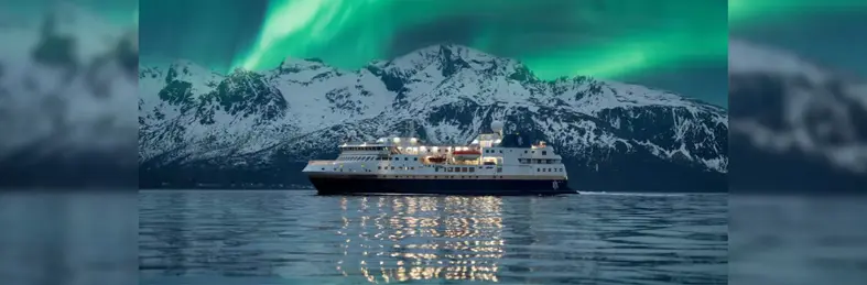 HX vessel in the sea before a snow-capped mountain with the Northern Lights overhead