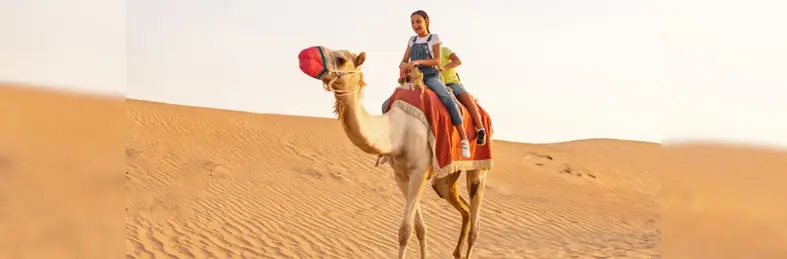 Young girl riding on the back of a camel in the desert