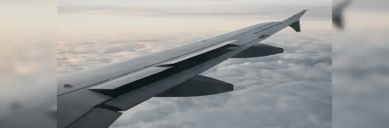 Wing of airplane flying over clouds at sundown