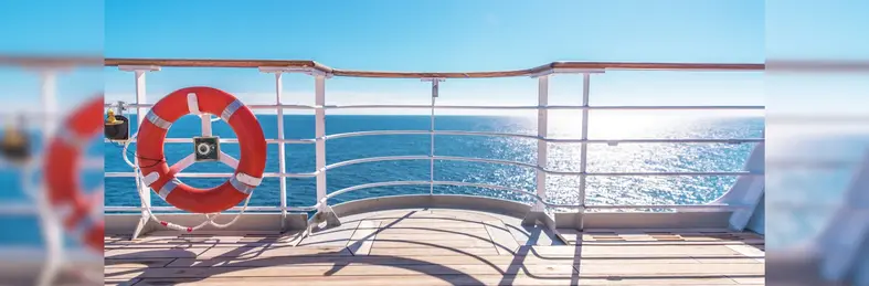 The deck of a cruise ship, with the sea and sun in the background and emergency life ring in the foreground.