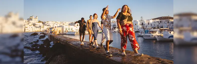 Four young travellers walking along the sea wall in Santorini, Greece.