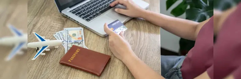 A person holding a credit card up to their laptop whilst booking a holiday.