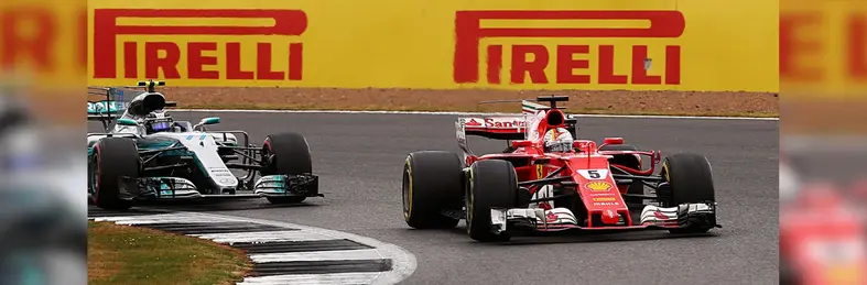 Two Formula 1 racecars turning a corner with Pirelli advertisement hoardings behind them.