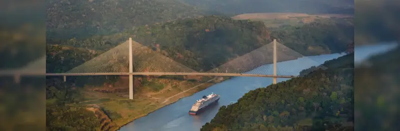 The Centennial Bridge spans the Culebra Cut of the Panama Canal as an Explora Journeys ship passes below, flanked by lush green hills.