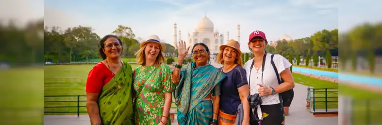 Five travellers waving in front of the Taj Mahal