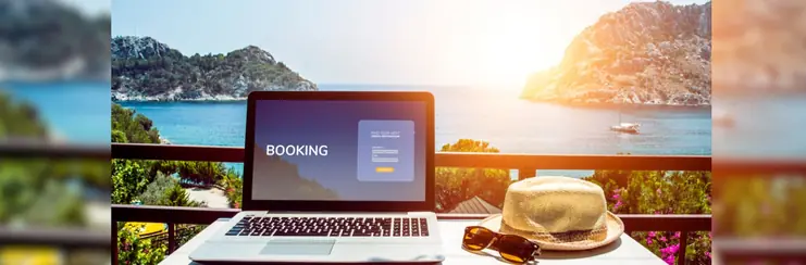 A laptop showing a booking screen with sunhat and sunglasses beside it