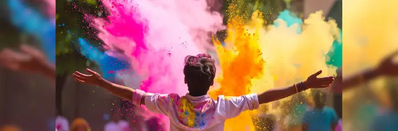 boy standing in front of different coloured powered paints at the Holi festival