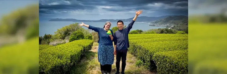 A lady and man posing in front of a rice field with the sea and hills in the background