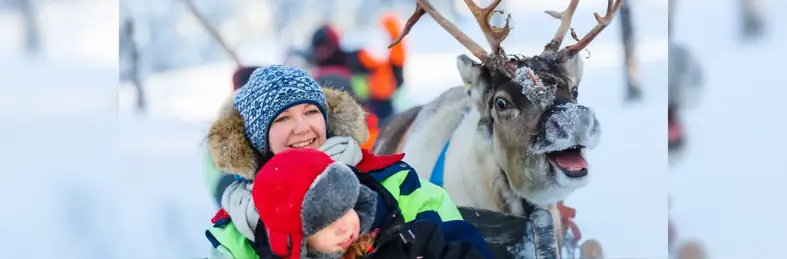 A mother, child and a smiling reindeer in the snow