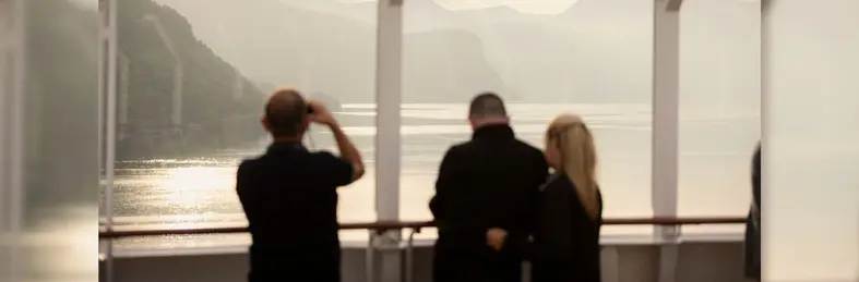 Three ship visitors looking out of the ship window for the fjords beyond