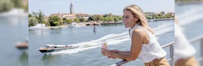 Woman gazing out of ship deck to the river below with a glass of prosecco in hand