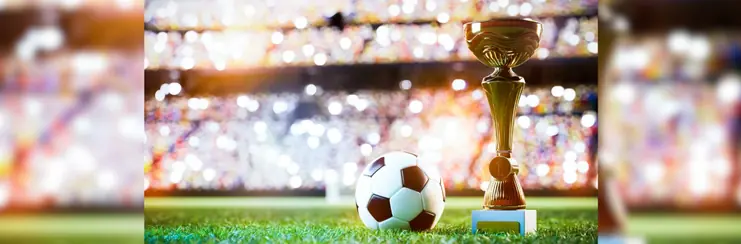 A glitzy photo of a football and a trophy together on a football pitch