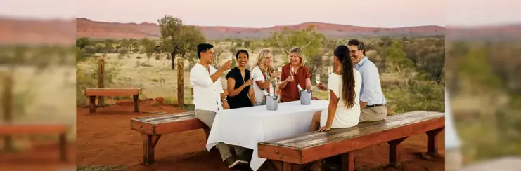 Six people sat around a table outside with the Outback in the distance