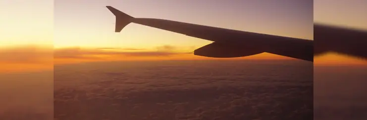 A photo of a plane wing flying over clouds during sunset