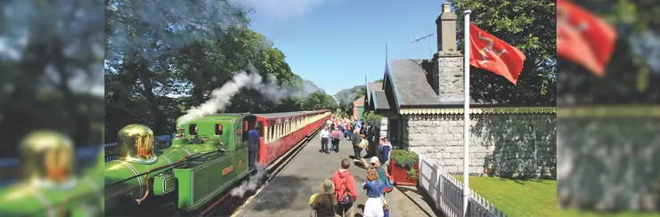 Steam train in Castletown, Isle of Man, with the Manx flag flying on a pole and people waiting to board