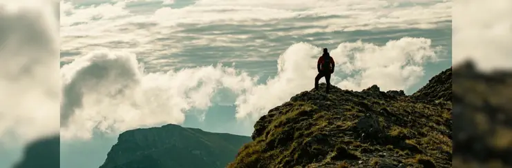 A man stood on top of a cliff looking out to the clouds