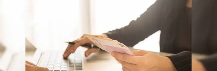 a hand taking money for a deposit with a laptop