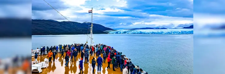 Cruise passengers standing at the front of the ship in front of a glacier