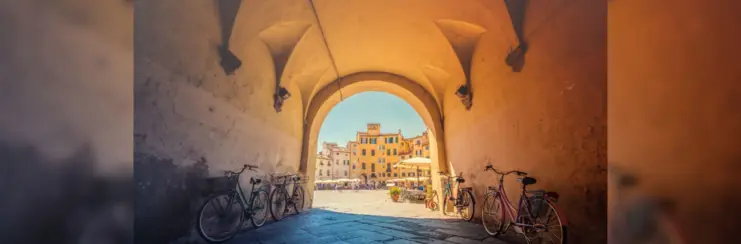 Bikes leaning on wall under archway by sunny town square