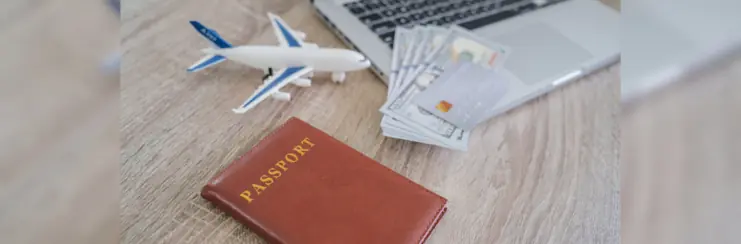 Passport, plane and travel money next to laptop on desk