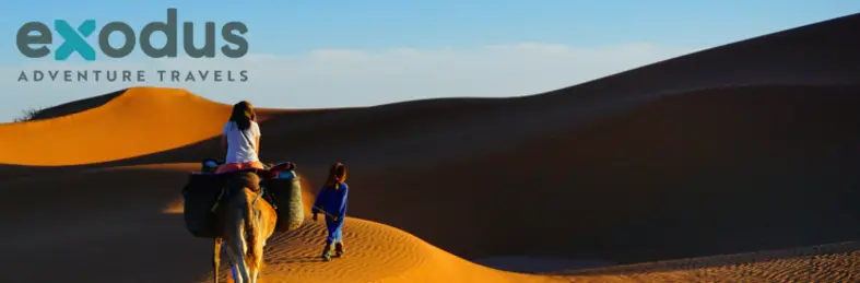 Guide leading guest on a camel through desert landscape with Exodus Adventure Travels logo overlaid on the top left cornerpng