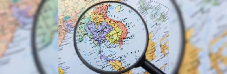 Magnifying glass looking at the Pacific Asia region on a map.